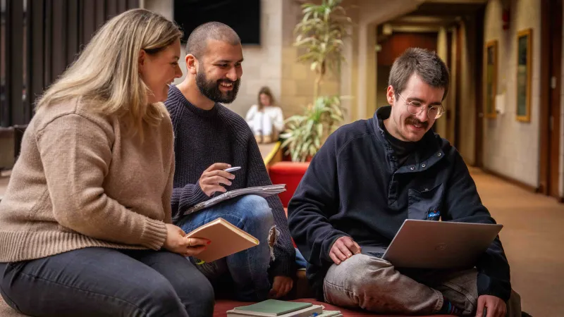 Three Department of Psychology students smiling and looking at a laptop