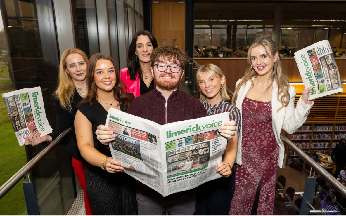 A group of six people in smart dress standing together and holding up newspapers