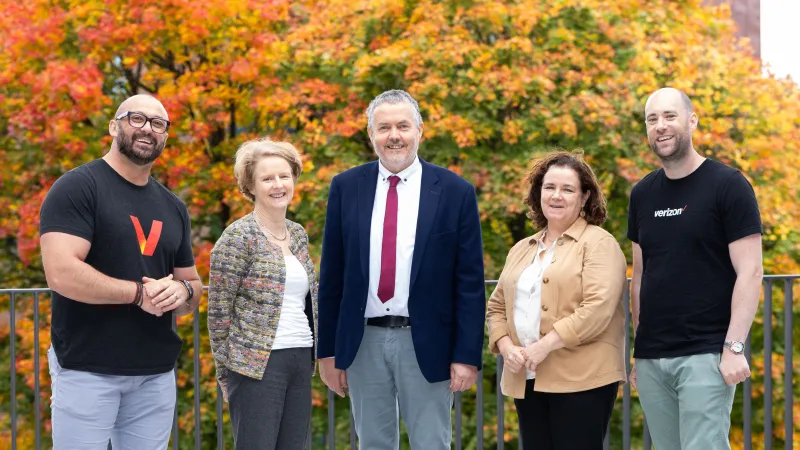 Five people standing on a balcony. There is a large tree in the background with orange and yellow leaves. From left to right: Keith McClelland, Senior Talent Acquisition Partner, Verizon; Professor Ann Ledwith, UL Interim Provost and Deputy President; Dr Chris McInerney, Director of UL's Transferable Skills Unit; Dr Sandra Joyce, Dean of UL's Faculty of Arts, Humanities and Social Sciences; Brian Cassidy, Senior Talent Acquisition Consultant, Verizon