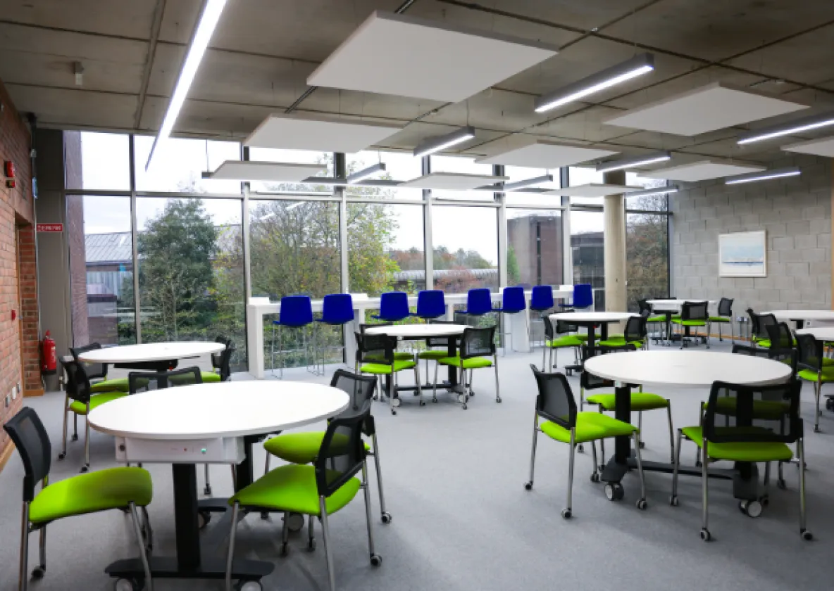 an empty room with tables and brightly coloured chairs with a large window