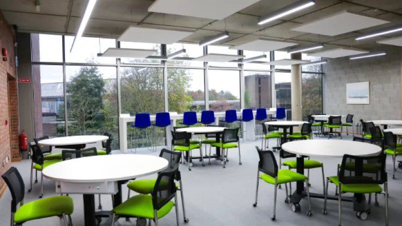 an empty room with tables and brightly coloured chairs with a large window
