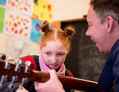 Man playing guitar with child looking at it