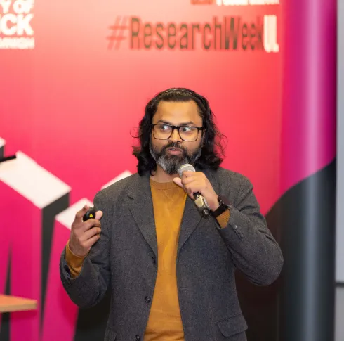Man with long hair and a bear holding a microphone giving a talk