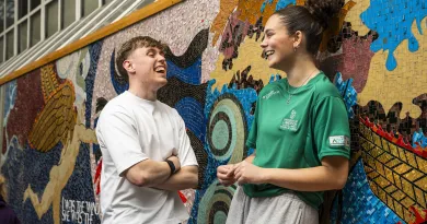 two students laughing in front of colourful wall mural