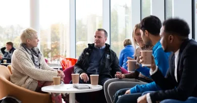 Four people of varying ages sitting and chatting with coffee