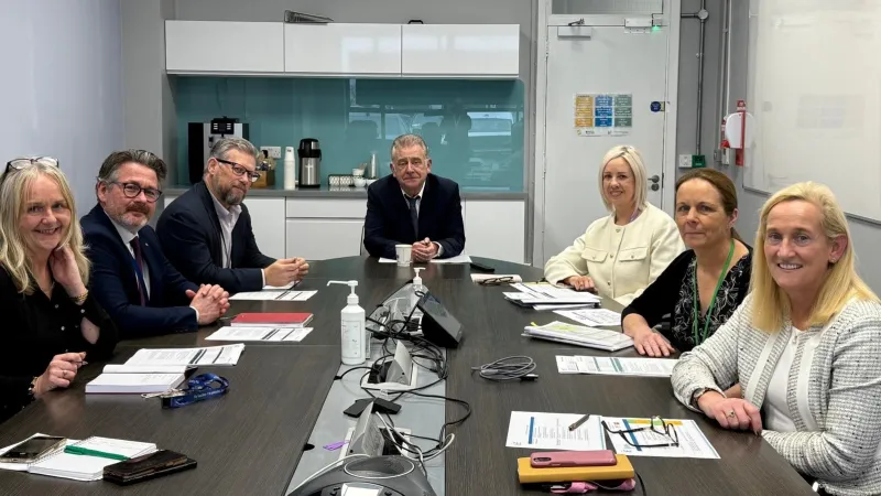 Representatives from UHL and UL in professional dress are pictured seated, smiling at the viewer, in a boardroom setting.